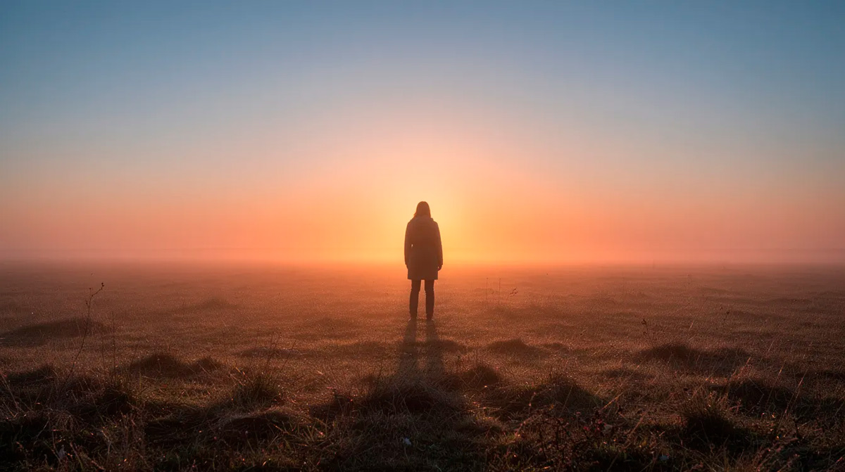Eine Person steht ruhig auf einem offenen Feld im Licht des Sonnenaufgangs und symbolisiert Klarheit, Neuanfang und innere Ausrichtung