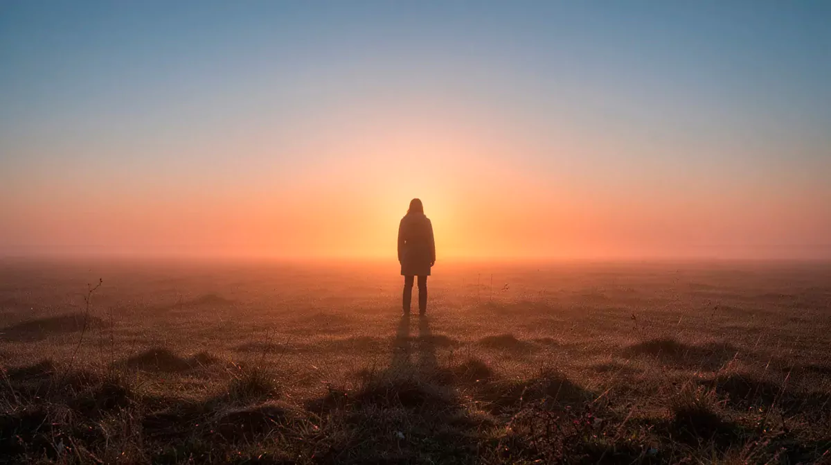 Eine Person steht ruhig auf einem offenen Feld im Licht des Sonnenaufgangs und symbolisiert Klarheit, Neuanfang und innere Ausrichtung